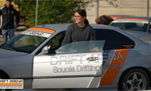 Persona in piedi accanto a un'auto argentata con adesivi arancioni e scritte "Drift Arena" e "Scuola Drifting".