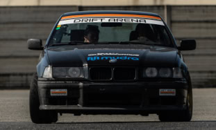 Auto da corsa nera su pista con adesivi sul parabrezza e sul cofano.