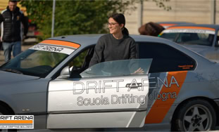 Persona in piedi accanto a un'auto argentata con adesivi arancioni e scritte "Drift Arena" e "Scuola Drifting".